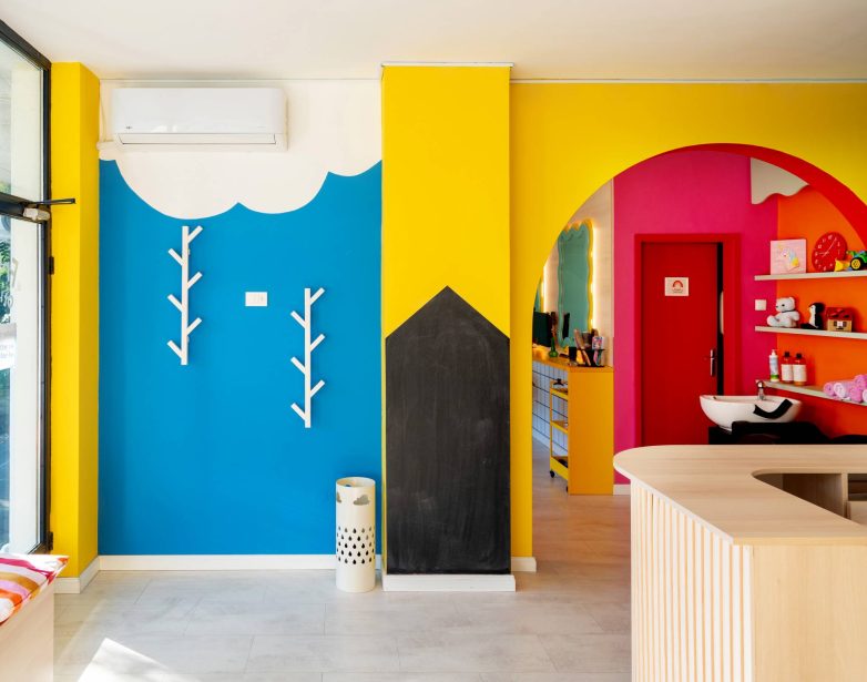 Dečji salon sa plavim zidom, ilustracijama i prolazom ka frizerskom delu u jarkim bojama