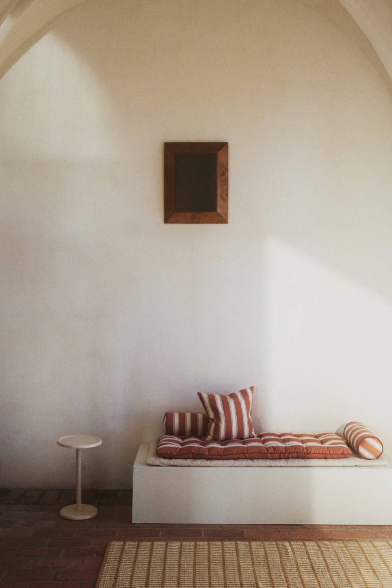 Veliki prošiveni jastuk za sedenje sa prugama postavljen na klupu uz dekorativne jastuke u enterijeru