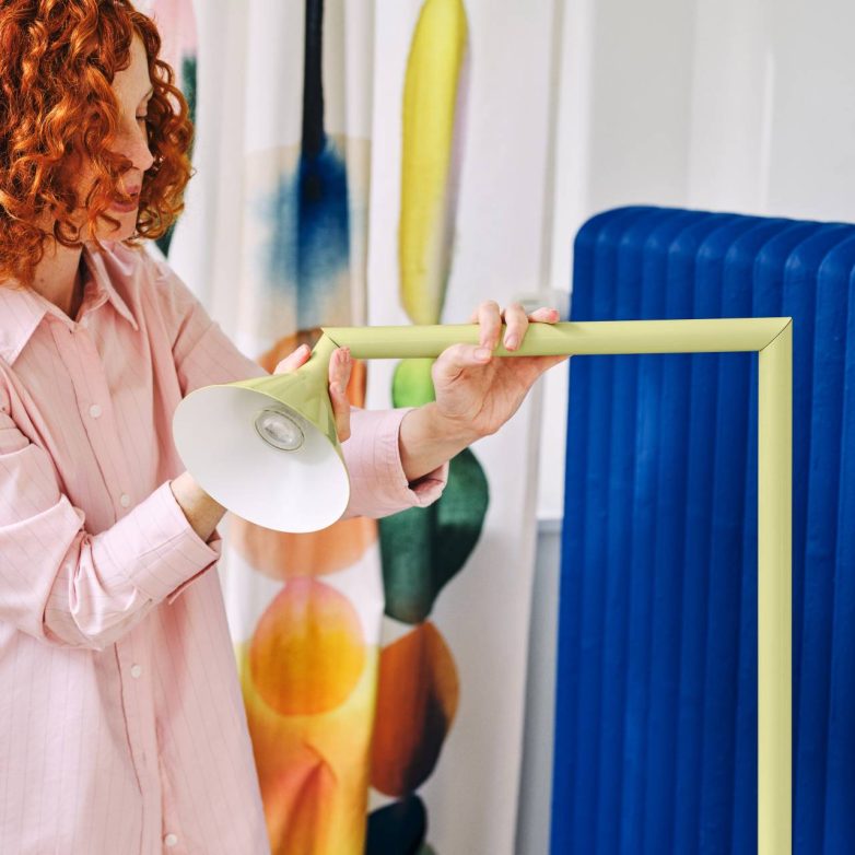 Osoba podešava svetlo na modernoj lampi sa rotirajućim krakom u svetlozelenoj boji