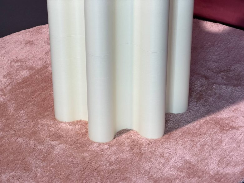 Detalj donjeg dela stalka za odeću sa talasastom formom koji stoji na roze tepihu tokom izložbe u Milanu