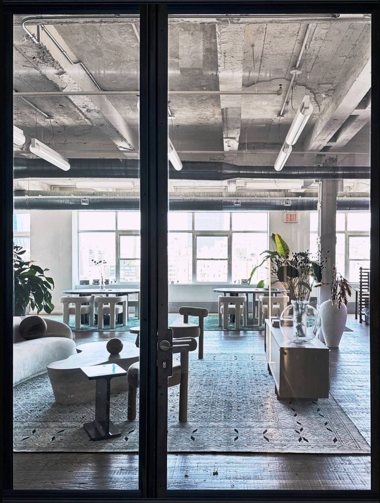 Pogled kroz staklena vrata na "lounge" zonu i radni prostor sa stolovima u kancelariji