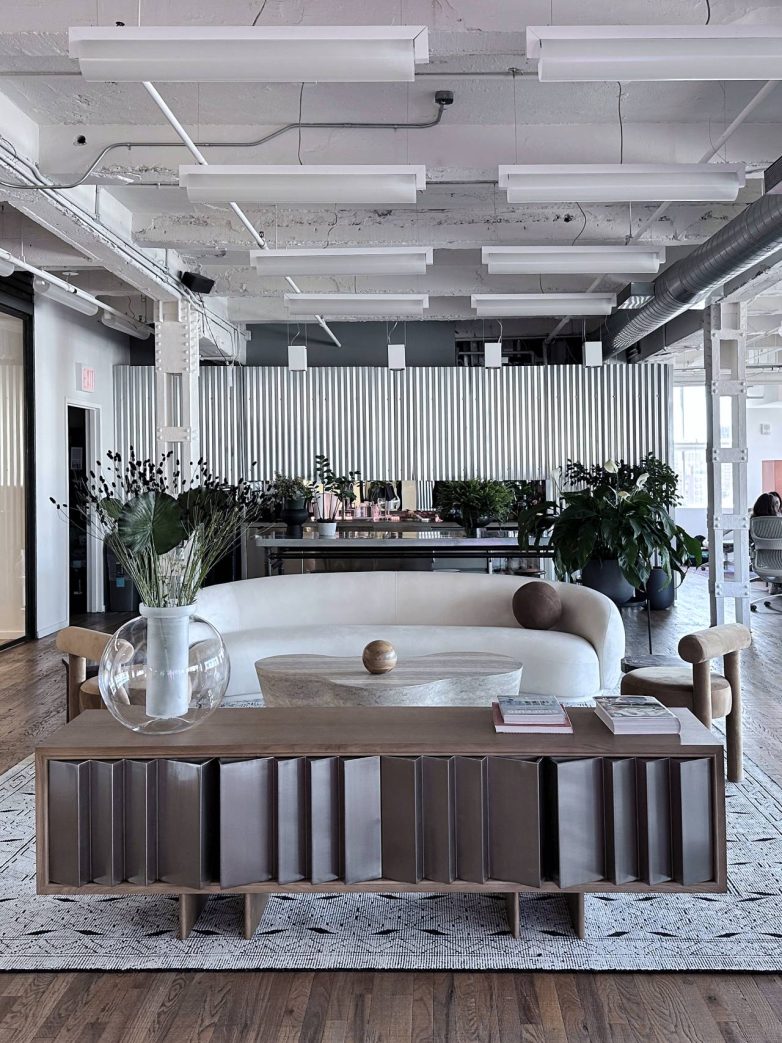 "Lounge" prostor kancelarije sa sofom, klub stolom, dekorativnim biljkama i industrijskim plafonom