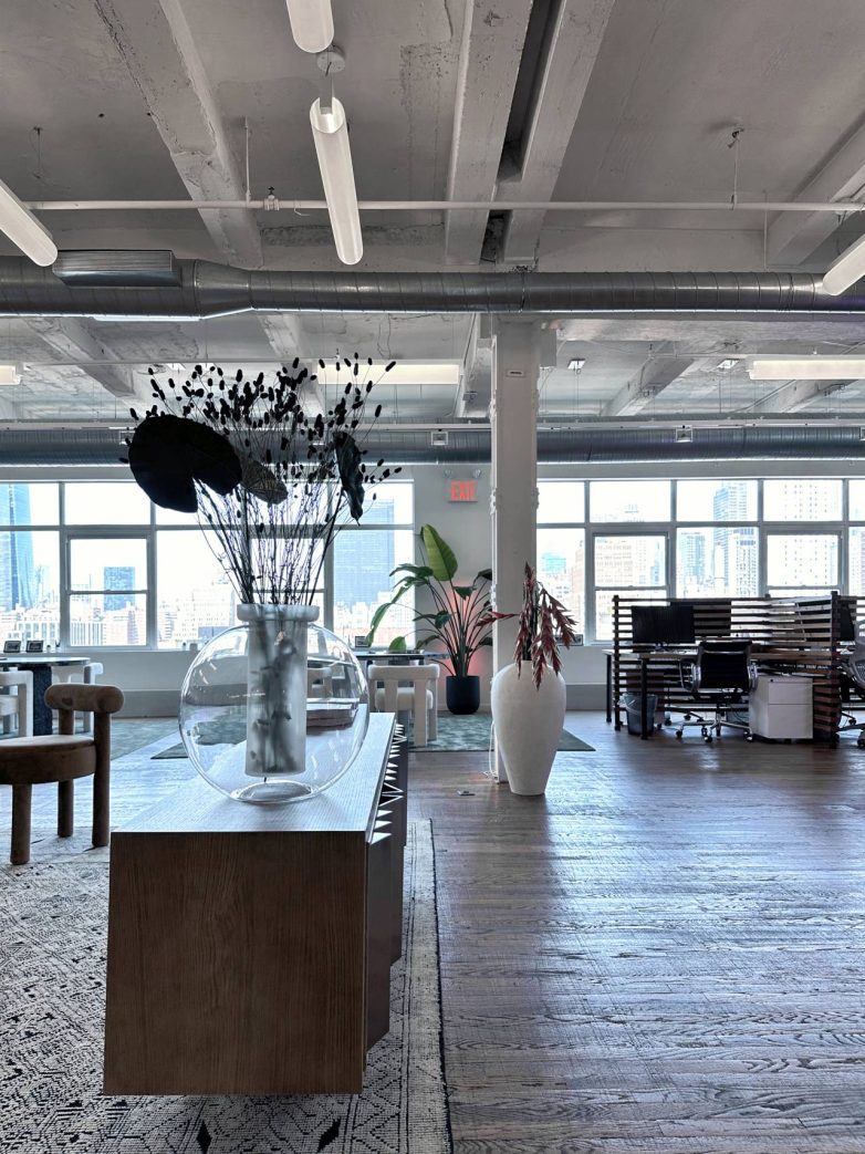 Velika staklena vaza sa biljkama u otvorenom kancelarijskom prostoru sa pogledom na grad