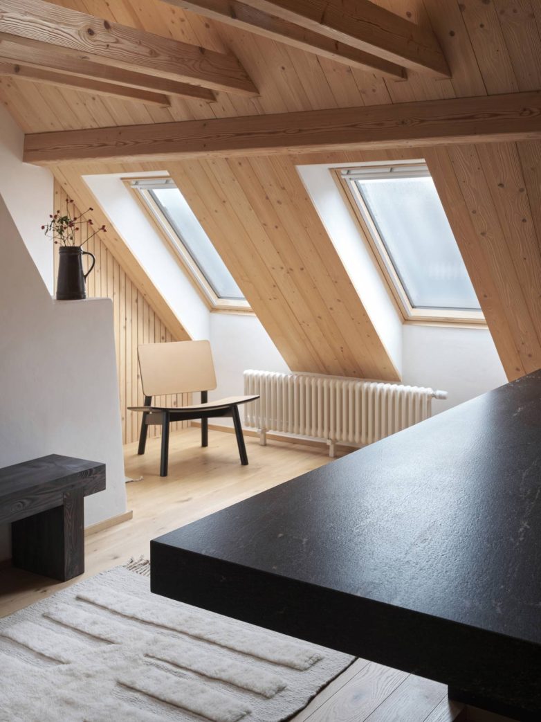Potkrovlje sa kosim krovom, krovnim prozorima, drvenim gredama i crnom granitnom površinom u prvom planu