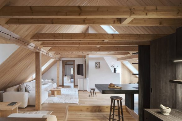 Svetao enterijer potkrovlja u češkoj kolibi sa vidljivim drvenim gredama, belom sofom i centralnim crnim šankom