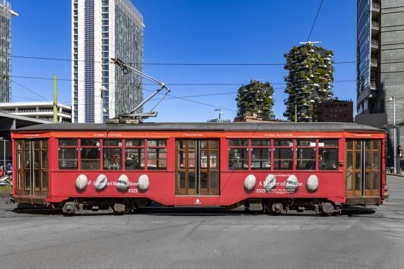 Crveni tramvaj sa natpisom Salone del Mobile Milano prolazi kroz grad sa modernim zgradama u pozadini
