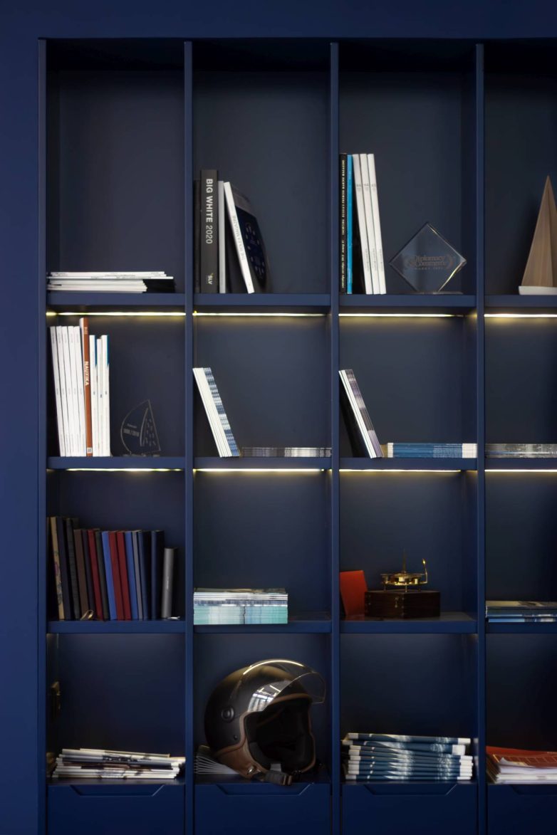 Ugradne police u salonu Yachting One u Beogradu sa knjigama, dekoracijom i integrisanom rasvetom u tamnoplavoj boji.