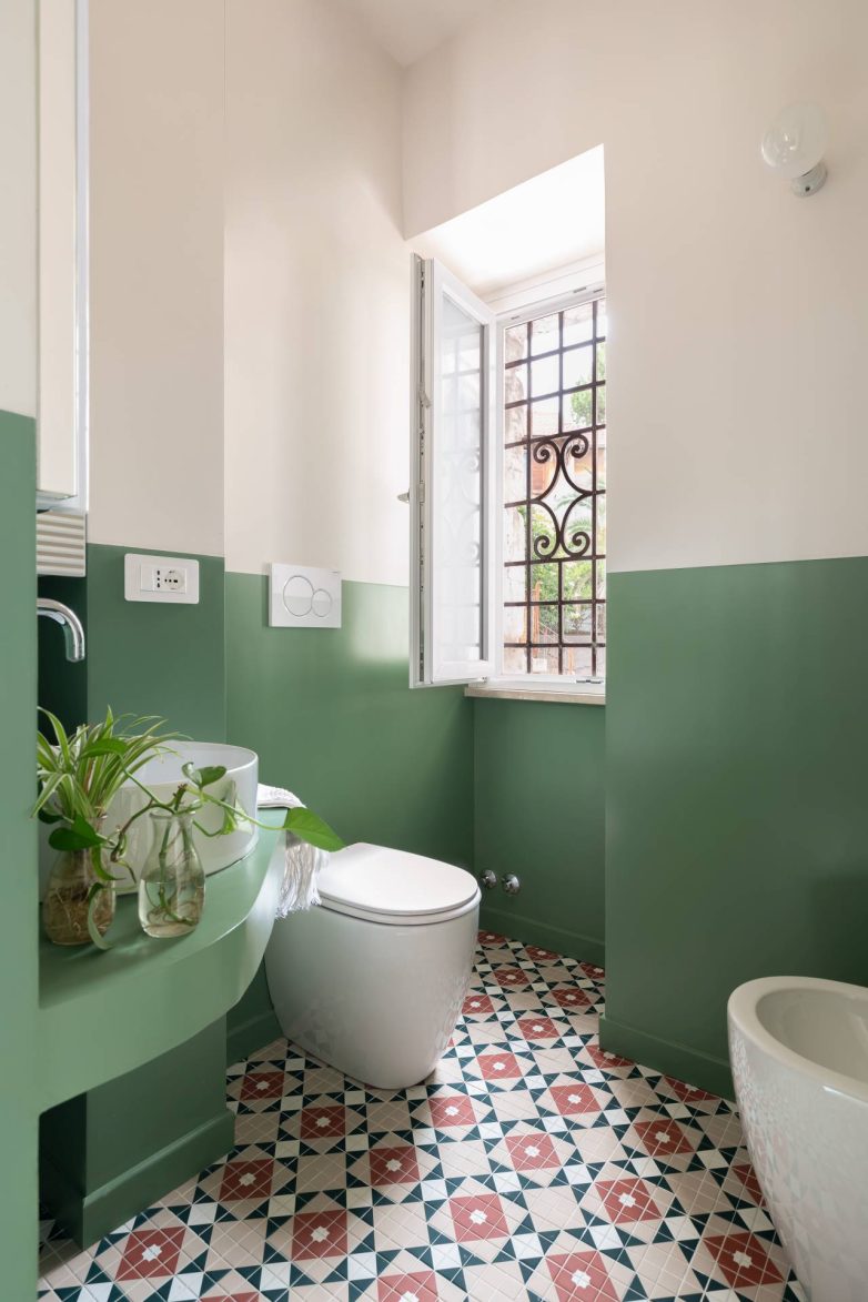 Kupatilo u stanu Casa Garbatella u Rimu ima zelene podloge od smole, prozor sa metalnom rešetkom i pod sa geometrijskim pločicama.