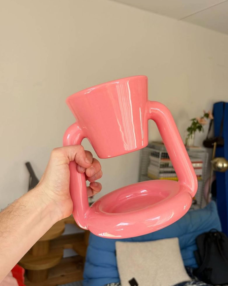 Roze Chunky Coffee Maker Gustafa Vestmana prikazan je u ruci, u enterijeru sa plavom sofom u pozadini.