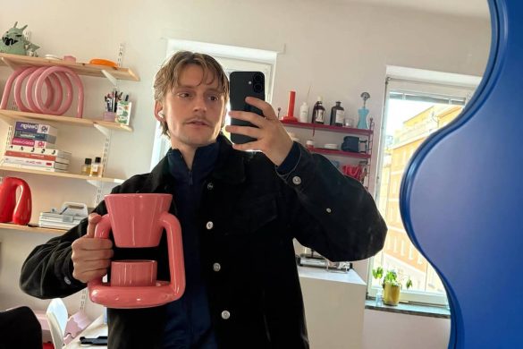 Gustaf Vestman drži roze Chunky Coffee Maker ispred ogledala u enterijeru sa šarenim policama i plavim ogledalom.