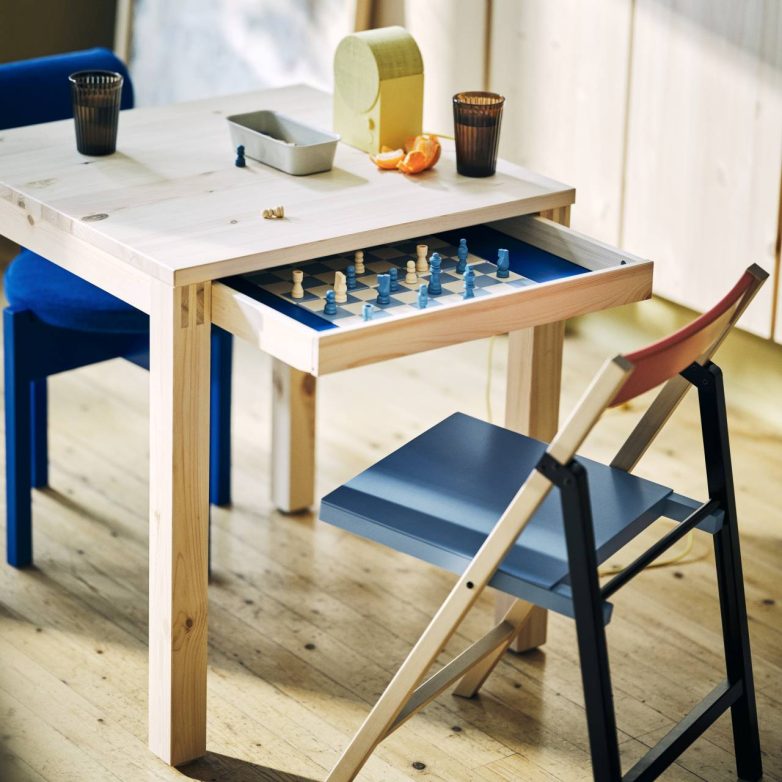 Drveni sto iz IKEA PS 2026 kolekcije ima izvučenu fioku sa šahovskom tablom i figurama