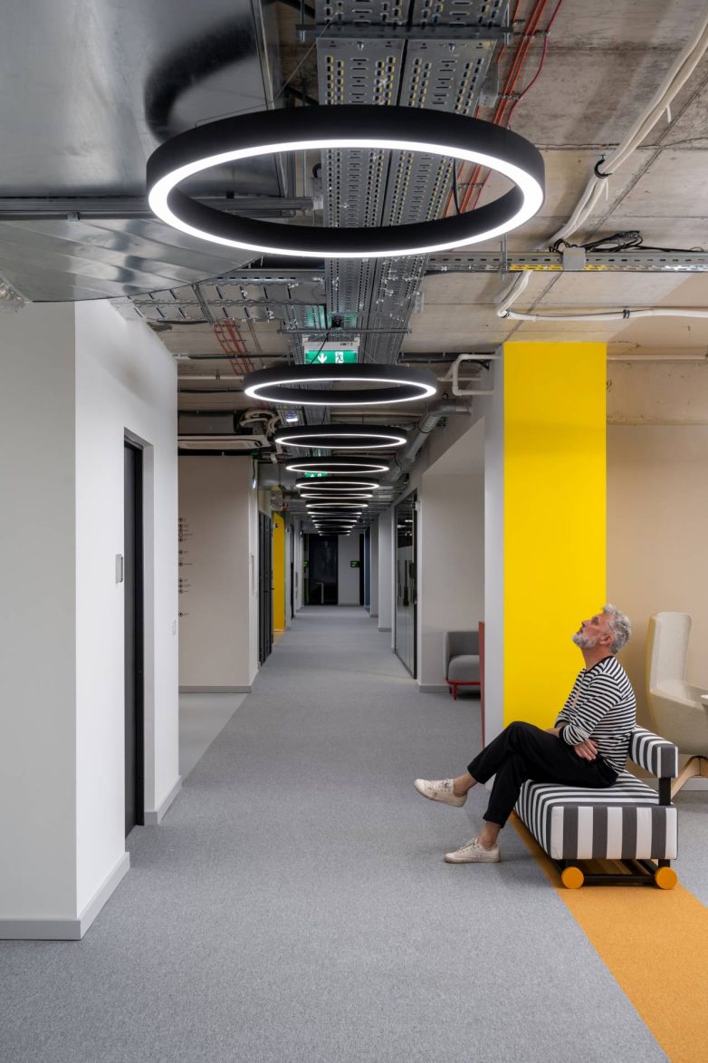 Hodnik u kancelariji kompanije Serb Tech u Beogradu ima niz kružnih svetiljki, otvorene instalacije na plafonu i žuti akcentovani zid.