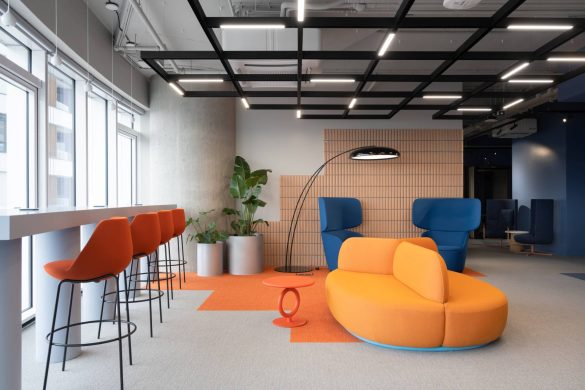 "Lounge" zona u enterijeru IT kancelarije u Beogradu ima narandžasti modularni kauč, plave fotelje, barske stolice i akcentovani zid od drveta.