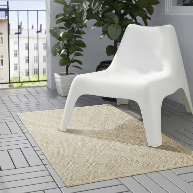 Neutralni IKEA tepih za terasu postavljen je ispod bele baštenske stolice na popločanom balkonu