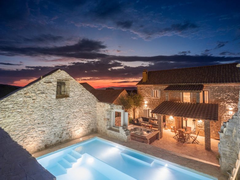 Bazen u dvorištu kamene kuće Casa M na Hvaru sa osvetljenom terasom i pogledom na zalazak sunca