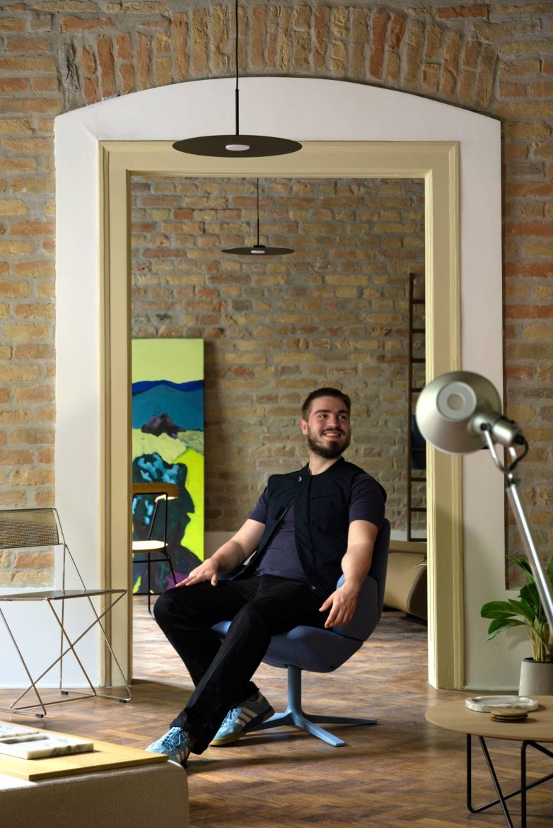 Bojan Ćirović u dizajnerskoj fotelji u FOUND.store "pop-up" prostoru u Beogradu, sa zidom od opeke, parketom i nameštajem u pozadini.