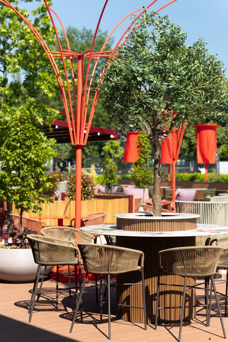 Bašta restorana GOAT u Banjoj Luci sa kružnim stolovima, pletenim barskim stolicama, drvećem, zelenilom i crvenim metalnim konstrukcijama, projekat studija JB architect