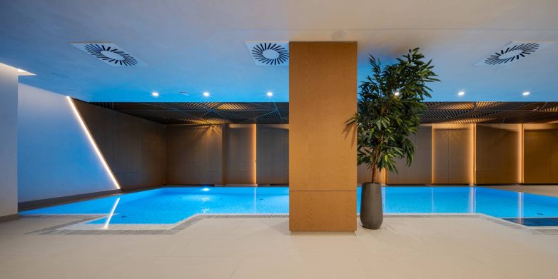 Pogled na SPA zonu u Zemunu sa bazenom, drvenim oblogama, centralnim stubom, biljkama, raster plafonom i linearnom rasvetom