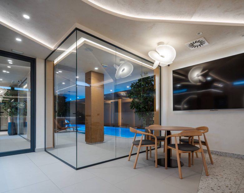 Kafe zona u okviru SPA enterijera u Zemunu, sa staklenim pregradama, pogledom na bazen, drvenim nameštajem i zaobljenom plafonskom rasvetom