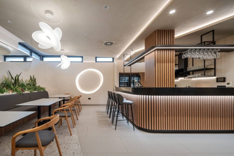 Kafe u okviru SPA zone u Zemunu sa šankom obloženim drvenim letvicama, visećom rasvetom, zelenilom i zaobljenim plafonskim linijama