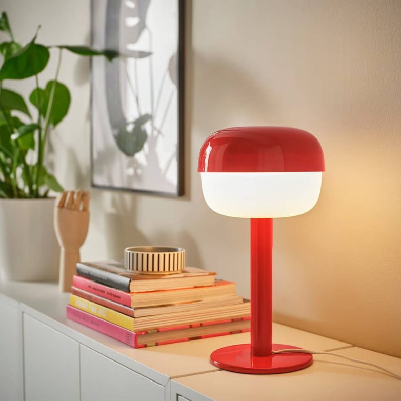 Crvena BLÅSVERK stona lampa na beloj komodi pored knjiga i biljke