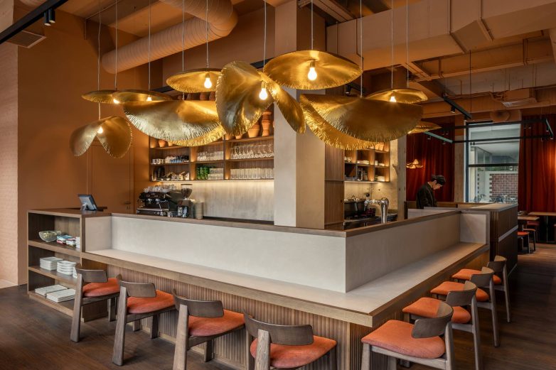 Centralni bar restorana Lucky Cat u Ljubljani sa velikim mesinganim visilicama, drvenim nameštajem i stolicama sa terakota sedištima