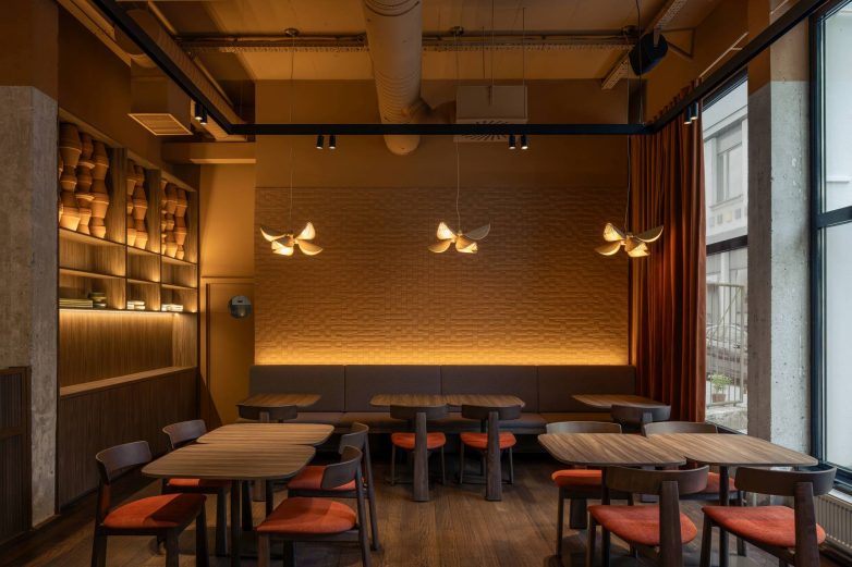 Enterijer restorana Lucky Cat u Ljubljani sa tapaciranom klupom, teksturisanim zidom, drvenim policama i visećim svetiljkama iznad stolova