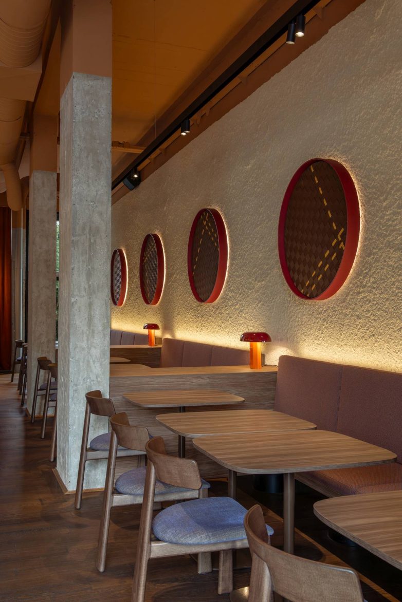 Enterijer restorana Lucky Cat u Ljubljani sa tapaciranom klupom, tekstilnim objektima u crvenim ramovima i grubim zidom sa pozadinskim osvetljenjem